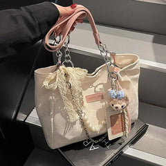 Tabletop close-up of cream canvas shoulder tote showing beaded handles, patches, and hardware.