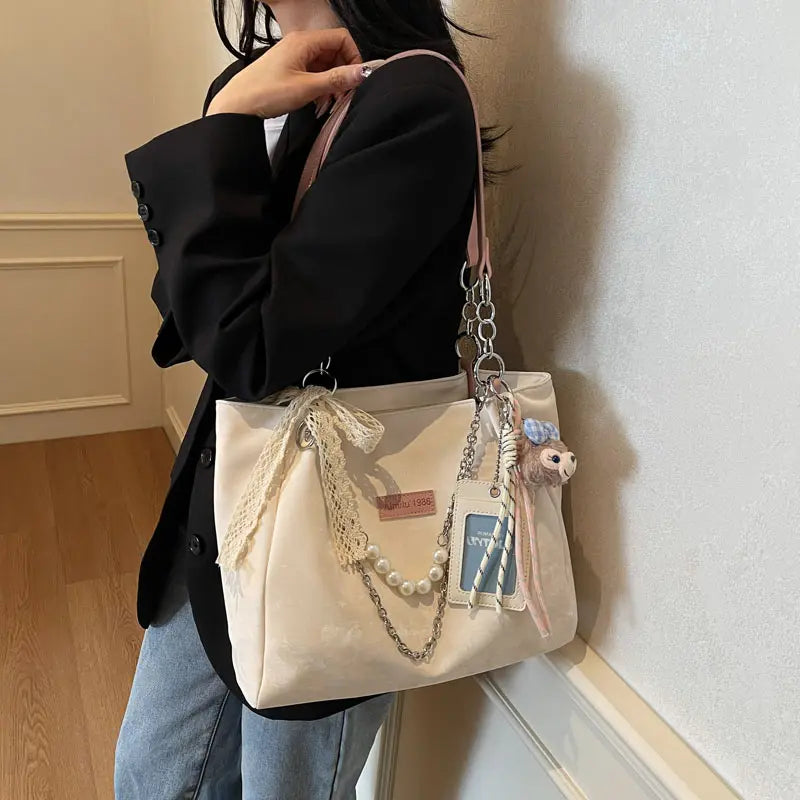 On-model cream canvas shoulder tote with pink beaded strap and patches, side view by wall.