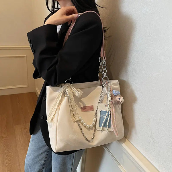 On-model cream canvas shoulder tote with pink beaded strap and patches, side view by wall.