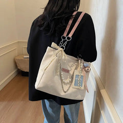Handheld cream canvas shoulder tote with beaded handle and teddy bear keychain on stairs.