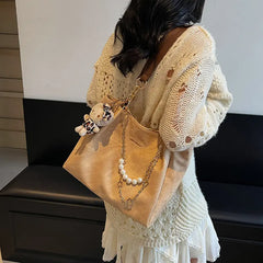 On-model tan canvas shoulder tote with pearl chain, held by hand at side.