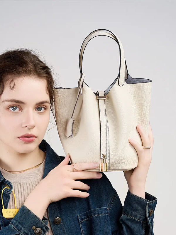 Model holding a Classic Leather Bucket Bag in a studio shot, showcasing its minimalist design and neutral tone.