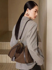 A woman wearing a grey blazer carries a Suede Crescent Shoulder Bag, showcasing its stylish design and functionality.