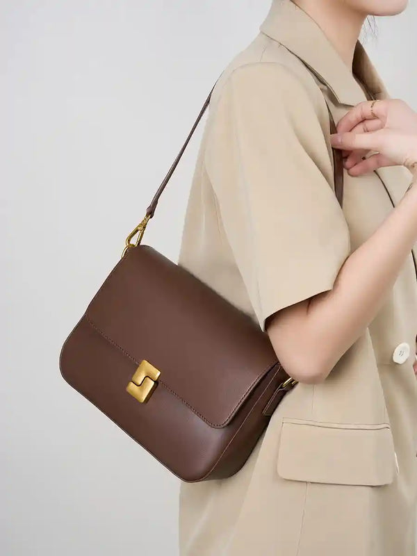 Minimalist Tofu Bag in brown leather worn as a shoulder bag with a sleek design and gold clasp, ideal for casual outings.