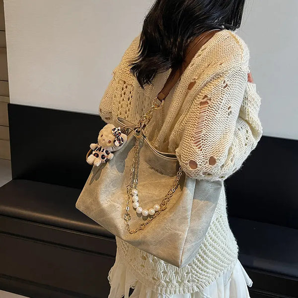 On-model tan canvas shoulder tote with pearl chain, side view while carried indoors.