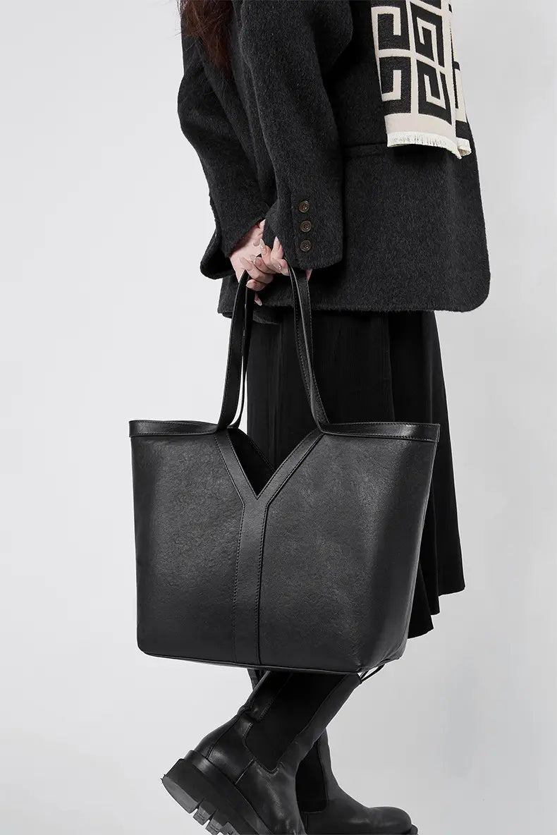 Large Leather Tote Bag held by a person wearing a black coat and skirt, showcasing its minimalist design and texture.