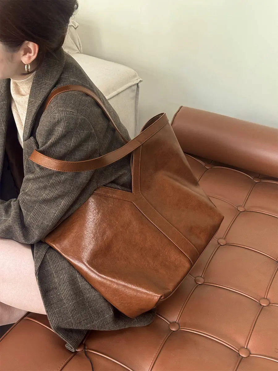 Large Leather Tote Bag displayed on a person sitting, showcasing its refined surface and minimalist design.