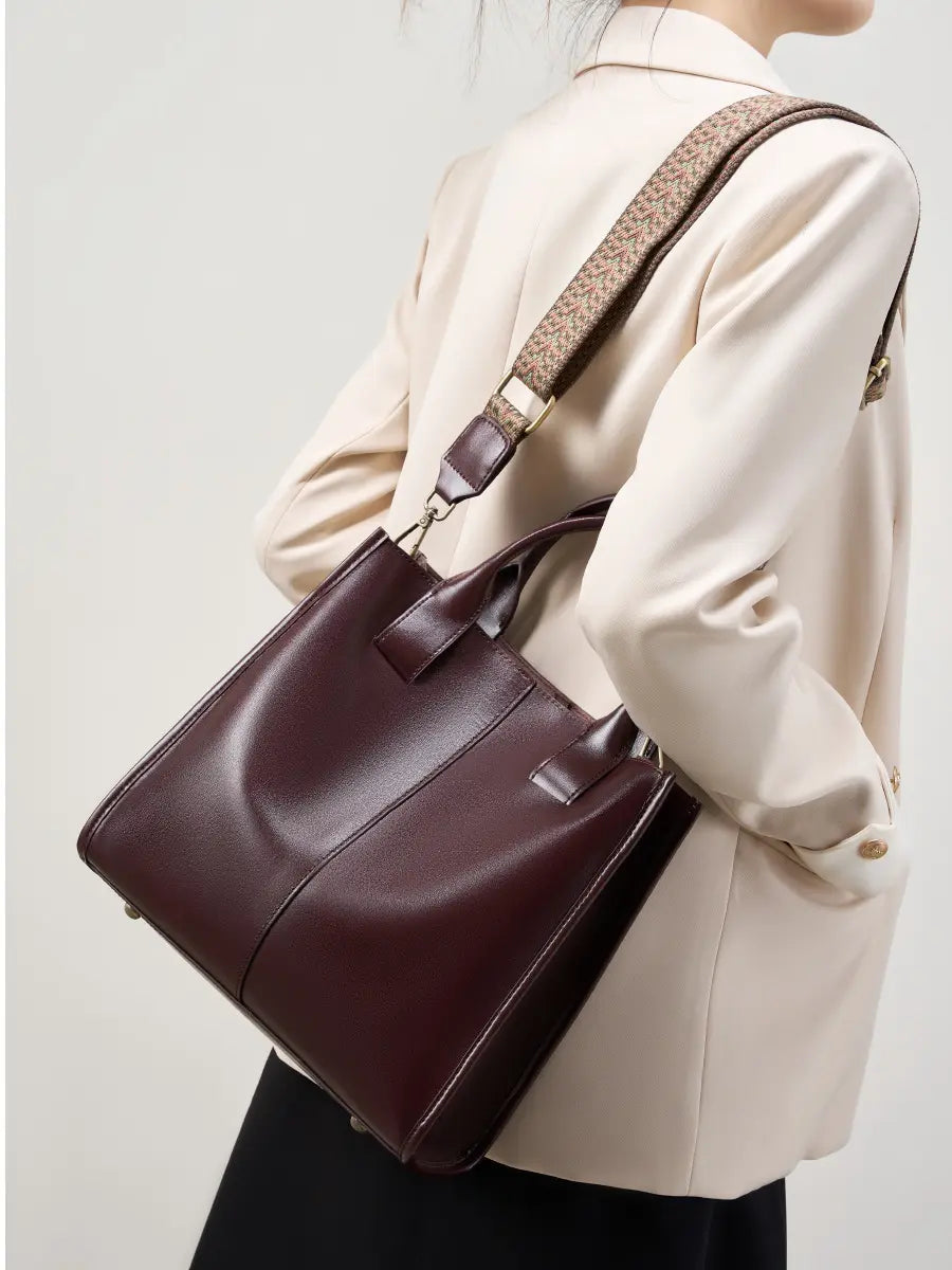 Top-Handle Leather Tote in burgundy with adjustable strap worn casually by a person in a stylish outfit.