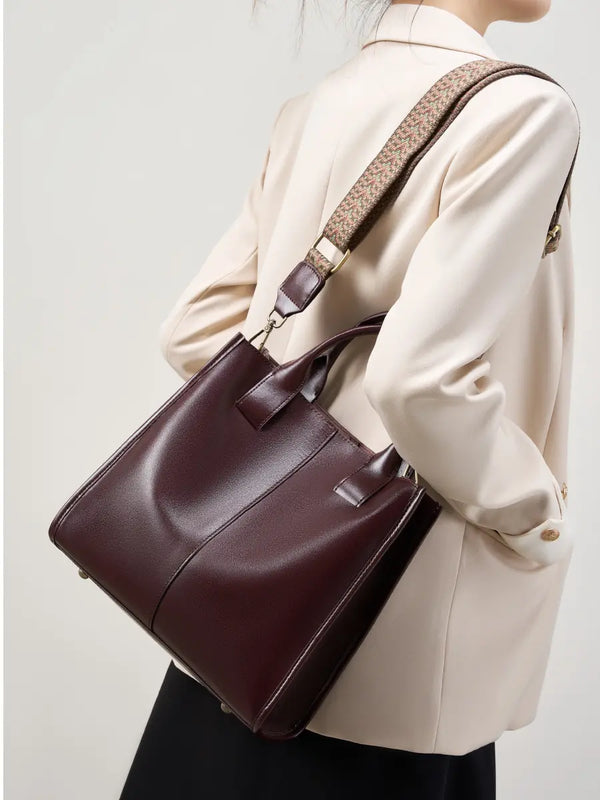 Top-Handle Leather Tote in burgundy with adjustable strap worn casually by a person in a stylish outfit.