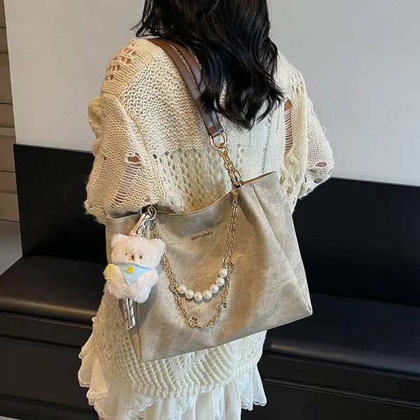 On-model beige canvas shoulder tote with pearl chain, slouchy hobo silhouette.