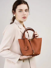 Classic Leather Bucket Bag displayed by a model in a neutral tone outfit, showcasing its minimalist design and top-handle.