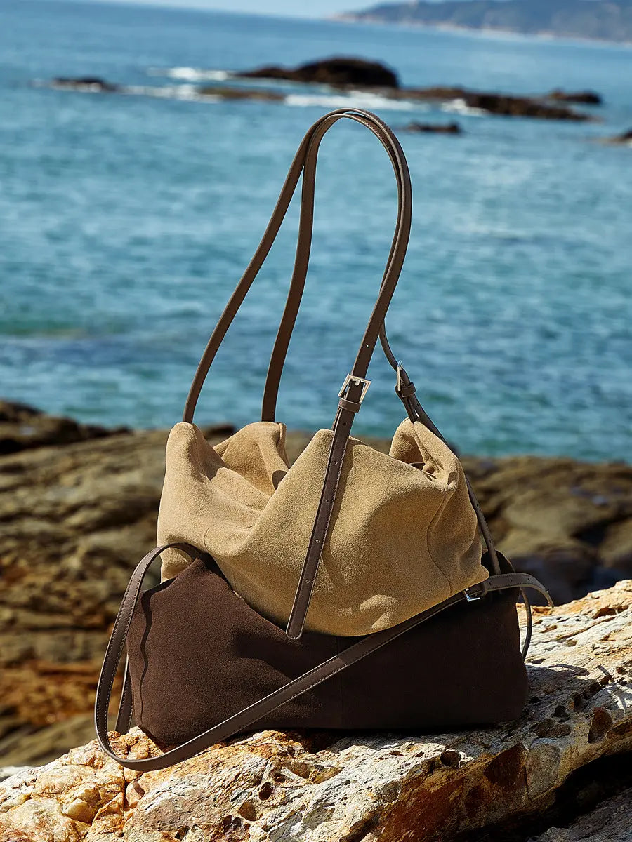 Suede Leather Pillow Hobo Bag displayed on a rocky beach, showcasing its stylish dual shoulder straps and chic silhouette.