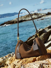 Suede Crescent Shoulder Bag displayed on rocky beach by the ocean, showcasing its stylish design and practical features.