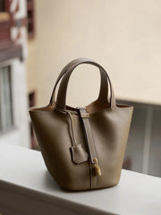 Classic Leather Bucket Bag in neutral tone with top-handle and drawstring, showcasing minimalist design in a lifestyle shot.