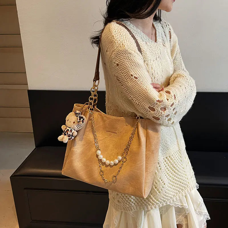 On-model tan canvas shoulder tote with pearl chain, shoulder carry, side view.