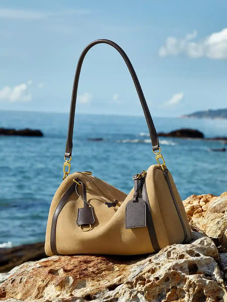 Suede Crescent Shoulder Bag on rocks by the ocean, showcasing a stylish mix of suede and leather with adjustable strap.