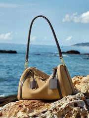 Suede Crescent Shoulder Bag on rocks by the ocean, showcasing a stylish mix of suede and leather with adjustable strap.