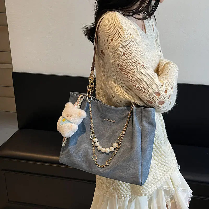 On-model gray canvas shoulder tote with pearl chain, partial body view.