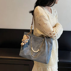 On-model gray canvas shoulder tote with pearl chain, shown at waist level.
