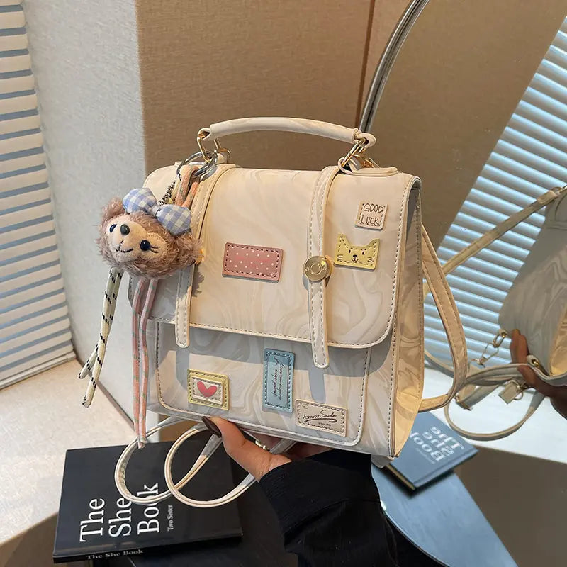 Tabletop view of cream patchwork mini backpack on blue bedding, front view with chain straps.