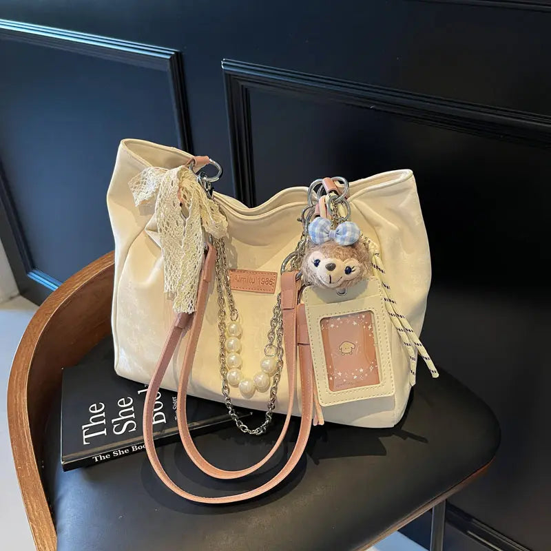 On-model cream canvas shoulder tote with beaded handles and teddy bear charm, front view at waist.