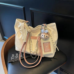 On-model cream canvas shoulder tote with beaded handles and teddy bear charm, front view at waist.