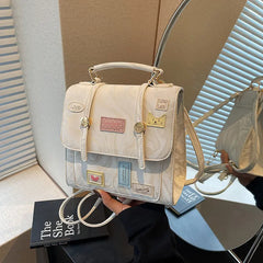 Tabletop close-up of cream patchwork mini backpack showing flap, buckle, and chain straps.