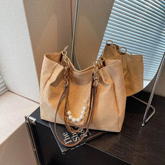 Close-up of tan canvas shoulder tote on tabletop, showing pearl chain and leather handles.
