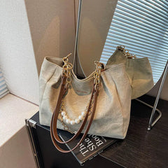 Close-up of tan canvas shoulder tote on tabletop, chain detail and handle attachments.