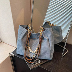 On-model tan canvas shoulder tote with pearl chain, side view while walking indoors.