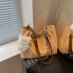 On-model tan canvas shoulder tote with pearl chain, shoulder carry, quarter angle.