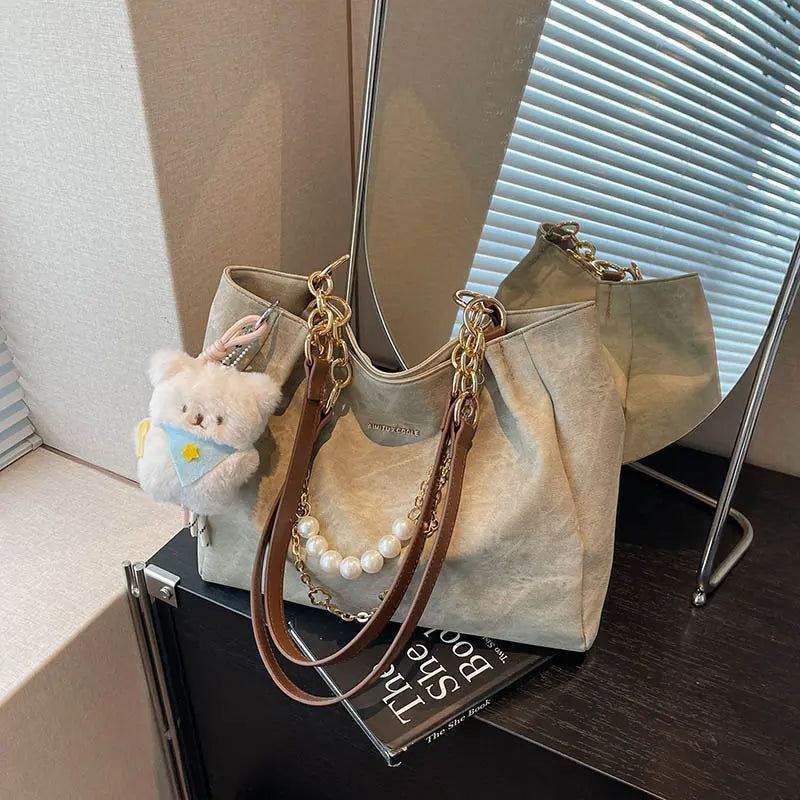 On-model tan canvas shoulder tote with pearl chain, held by hand at thigh level.