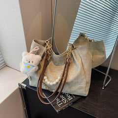 On-model tan canvas shoulder tote with pearl chain, held by hand at thigh level.
