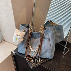On-model tan canvas shoulder tote with pearl chain, front view at hip, casual pose.