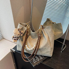 On-model tan canvas shoulder tote with pearl chain, seated pose, bag resting at side.