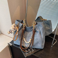 On-model cream canvas shoulder tote with beaded handle and teddy bear charm, carried at side indoors.